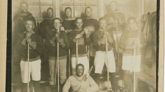 Group portrait of the Africville Sea-Sides hockey team in 1922, showing Black players arranged in rows indoors, dressed in early hockey uniforms and holding long wooden sticks.