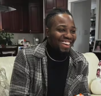 Isaac Downey smiling while seated indoors in a home setting.